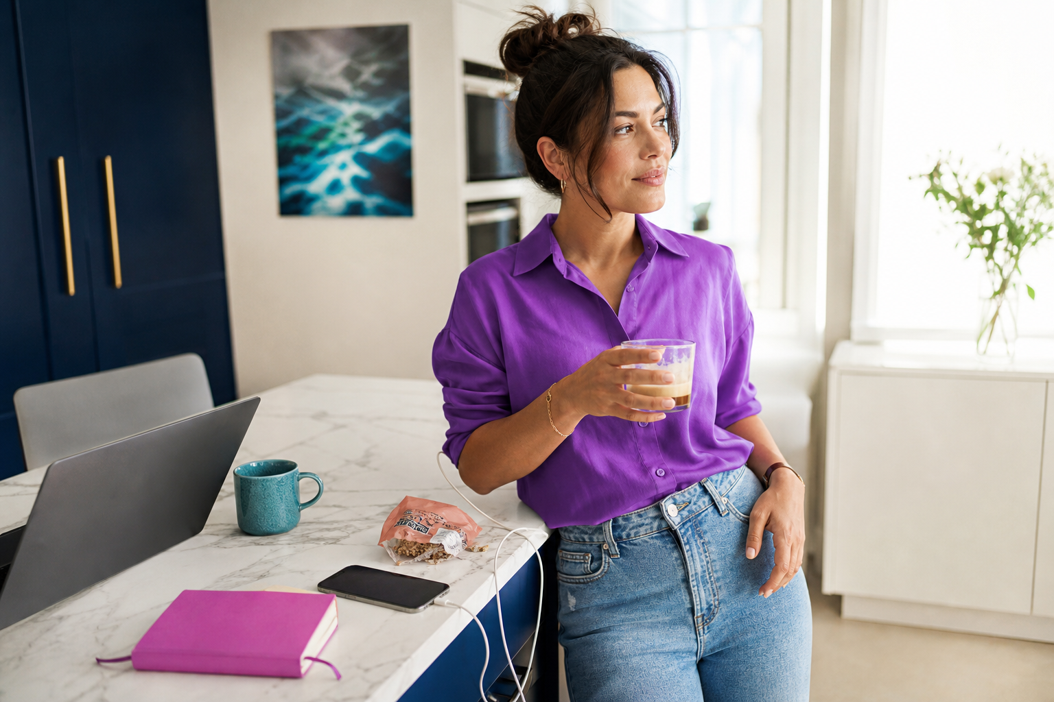 Vrouw in paarse blouse staat in een lichte keuken met een glas koffie naast een laptop en notitieboek.